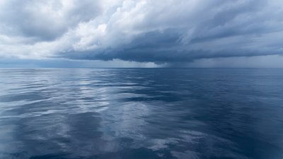 Eine spiegelglatte Meeresoberfläche, der Himmel ist bewölkt, am Horizont zeichnet sich ein Gewitter ab.