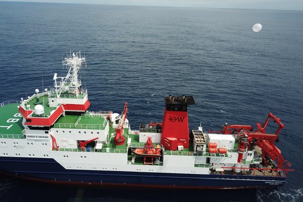 The research vessel Maria S. Merian on the open sea, photographed from above. A balloon with a radiosonde rises into the sky at the stern.