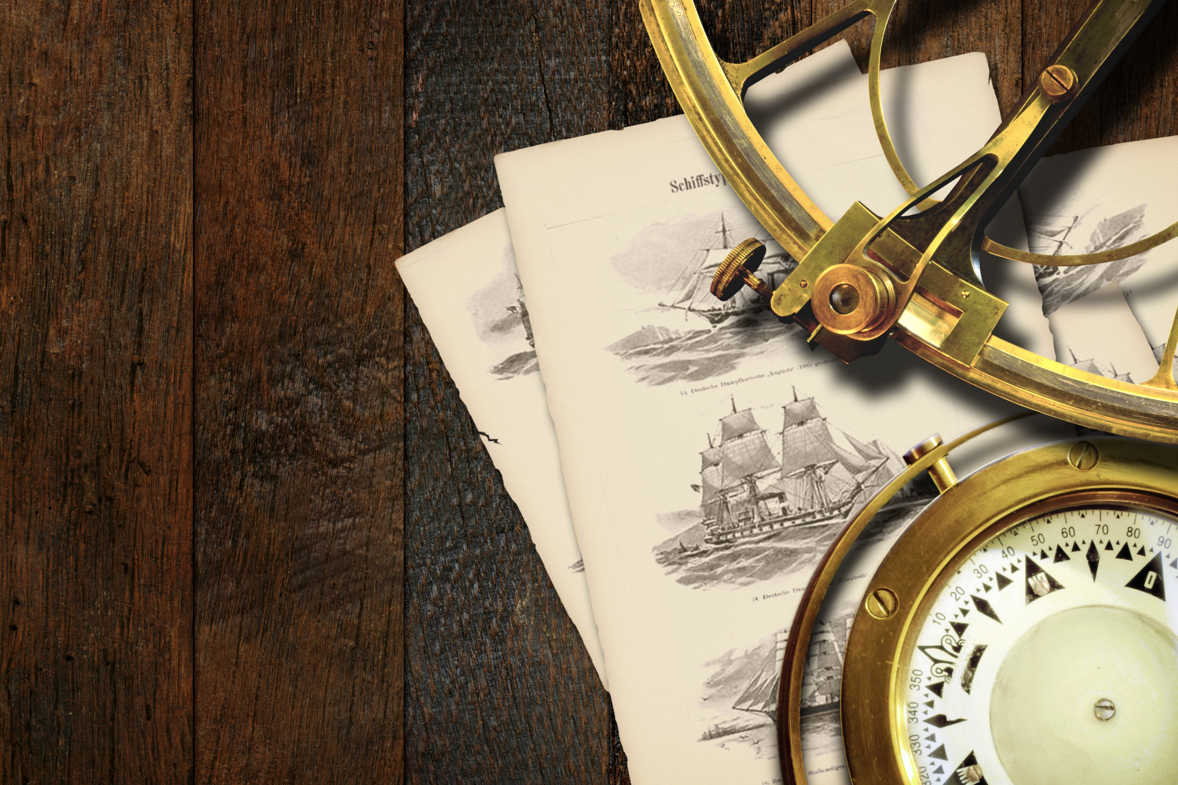 Historisches Navigationsset auf einem Holztisch: Ein goldener Sextant, ein Kompass und alte, illustrierte Seiten mit Segelschiffen und dem deutschen Titel "Schiffstypen" liegen auf dunklem Holz.