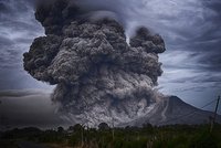 Volcanic eruption with towering ash cloud, forest and road in the foreground