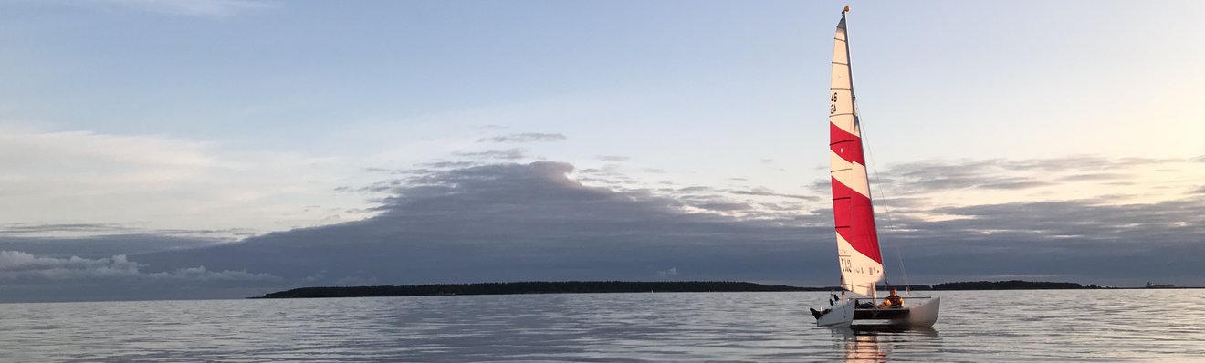 Doldrums in Tallinn bay. Catamaran on the water at sunset with island in the background.