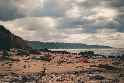 Ein mit Plastik verschmutzter Strand im Sonnenschein, der Himmel ist bewölkt.