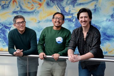 Chao Li, Hans Segura and Noel Brizuela at the Max Planck Institute for Meteorology. They are standing at a railing in front of a large-format, aesthetic visualisation.