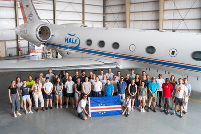 A group of scientists is gathered in a hangar in front of the aircraft HALO.